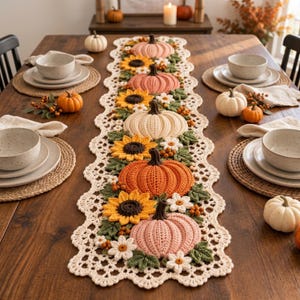 May include: A long, rectangular crochet table runner featuring a cream-colored scalloped border. The runner is decorated with a repeating pattern of crocheted pumpkins in shades of orange, pink, and cream, interspersed with yellow sunflowers, white daisies, and green leaves.