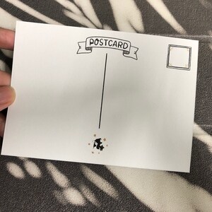 May include: A blank white postcard with the word "POSTCARD" written in black cursive on a banner at the top. A black and white illustration of a bat flying with gold stars is at the bottom. There is a blank space for a stamp in the upper right corner.
