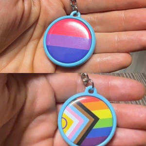 May include: A round keychain with a light blue border. The top keychain has a pink, purple, and blue design. The bottom keychain has a rainbow design with a brown, white, and yellow chevron.