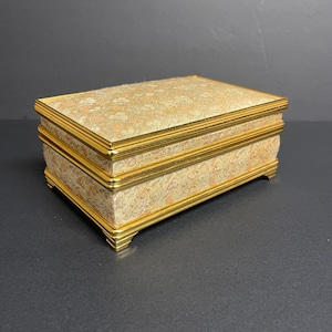 Könnte beinhalten: Eine Schmuckschatulle mit goldenen Verzierungen und einem Blumenmuster auf Deckel und Seiten. Die Schachtel hat drei Ebenen.