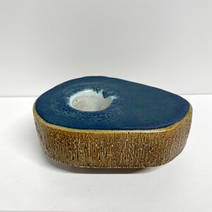May include: A blue and brown ceramic candle holder with a textured base and a round opening for a candle.