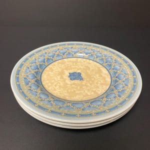 May include: A stack of three ceramic plates. Each plate features a light blue border with a repeating pattern, surrounding a beige center with a floral design and a blue floral accent.