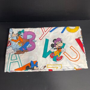 K&ouml;nnte beinhalten: Ein wei&szlig;es Bettlaken in Zwillingsgr&ouml;&szlig;e mit einem bunten Alphabetdruck mit Mickey Mouse, Minnie Mouse und Goofy. Die Buchstaben sind in verschiedenen Farben, darunter Rot, Blau, Gr&uuml;n, Gelb und Lila.