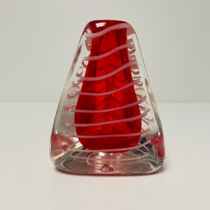 May include: A clear glass vase with a red and white swirl design. The vase is shaped like a triangle and has a small opening at the top.