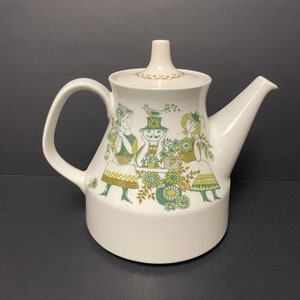 May include: White ceramic teapot with a lid, featuring a whimsical design of figures in green and gold. The teapot has a curved handle and a spout, perfect for serving tea. The design includes floral and human figures.
