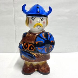 Peut inclure: Une figurine en céramique d'un guerrier viking portant un casque bleu avec des cornes et tenant un bouclier avec un motif bleu et noir.