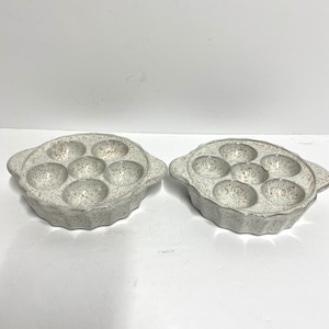 May include: Two white ceramic ramekin dishes with speckled brown glaze. Each dish has six individual round indentations and two handles.