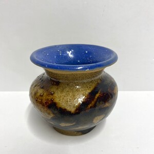May include: A small, brown and black ceramic vase with a blue rim. The vase has a speckled glaze and a rounded body.