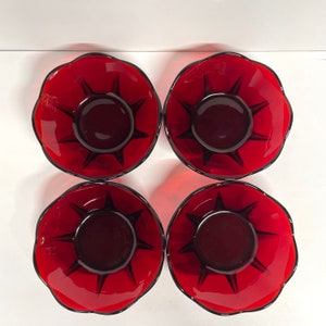 Peut inclure: Quatre bols en verre rouge avec un motif d'éclat d'étoile au centre. Les bols ont un bord festonné et un centre rouge foncé. Le motif en étoile est noir. Les bols sont disposés en carré.
