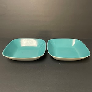 Può includere: Due ciotole quadrate in ceramica blu turchese con bordi bianchi. Le ciotole sono vuote e sono appoggiate su una superficie nera.