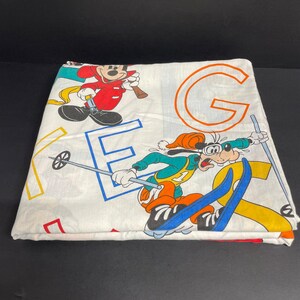 K&ouml;nnte beinhalten: Wei&szlig;es Bettlaken in Zwillingsgr&ouml;&szlig;e mit einem bunten Druck von Mickey Mouse und Goofy beim Skifahren. Das Laken zeigt die Buchstaben E und G in einer bunten Schrift.