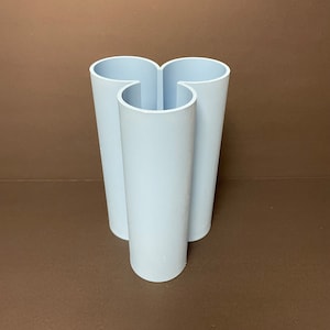 Puede incluir: Un jarrón de cerámica azul claro con tres aberturas, con forma de trébol.