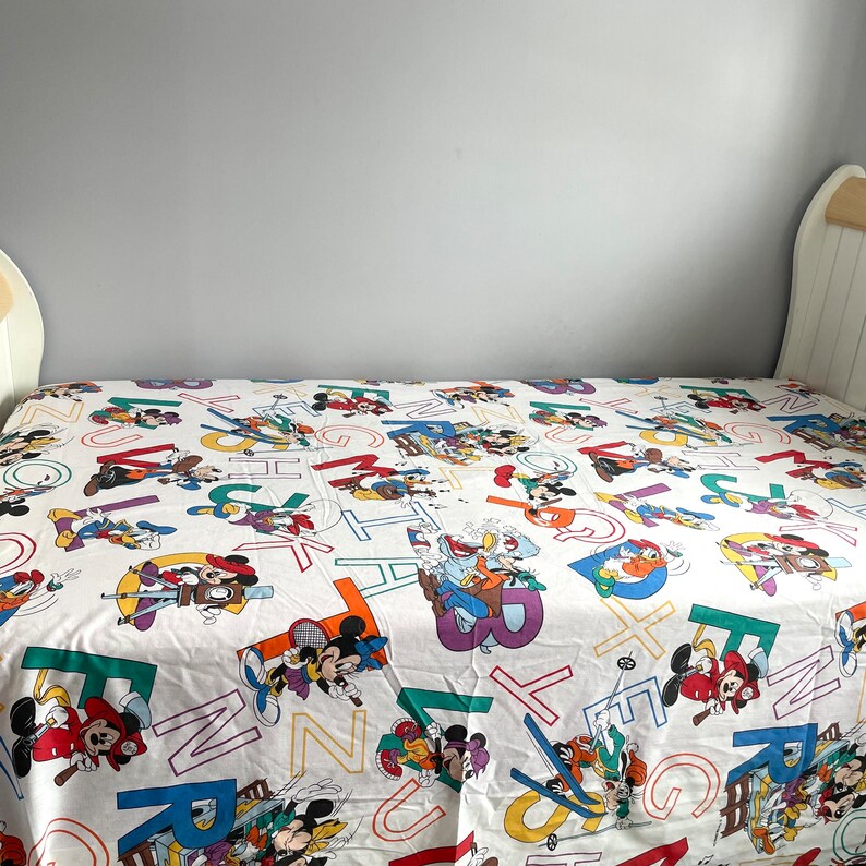 K&ouml;nnte beinhalten: Ein wei&szlig;er Bettbezug in Zwillingsgr&ouml;&szlig;e mit einem bunten Alphabetdruck mit Mickey Mouse und anderen Disney-Charakteren. Der Druck enth&auml;lt die Buchstaben A bis Z.