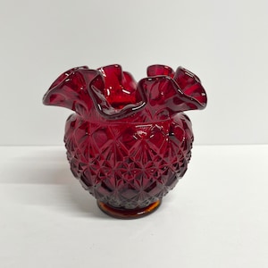 Peut inclure: Un vase en verre rouge avec un dessus à volants et un motif en diamant. Le vase a une base ambrée transparente.
