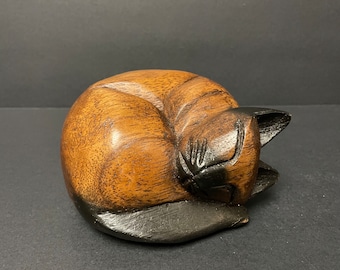 Estatueta vintage de gato de madeira maciça, representando um gatinho dormindo, com rosto e patas pintados à mão. Ideal para decoração de lareira, um presente rústico perfeito para amantes de gatos. Mede 7,3 cm (2 7/8”).