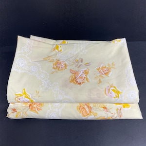 Puede incluir: Un juego de dos sábanas de cama amarillas con estampado floral y un patrón de encaje blanco. Las sábanas presentan un diseño floral con rosas amarillas y naranjas.