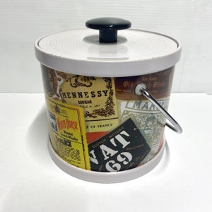 May include: White metal ice bucket with a white lid and a black handle. The bucket is decorated with various liquor labels, including Hennessy Cognac, White Horse Scotch Whisky, and Vat 69 Scotch Whisky.