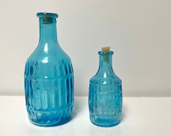 Peut inclure: Deux bouteilles en verre bleu avec des surfaces texturées et des bouchons en liège. Les bouteilles sont de tailles différentes.