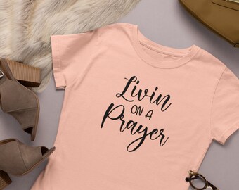 Peut inclure: Un t-shirt couleur pêche avec le texte "Livin on a Prayer" en lettres cursives noires.