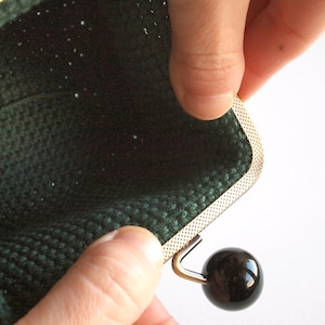 May include: A green crocheted coin purse with a silver metal frame and a black button closure.