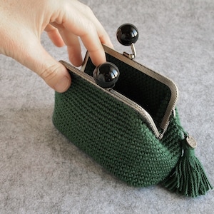 May include: A green crocheted coin purse with a black tassel and a silver clasp. The purse is open and the inside is lined with black fabric.