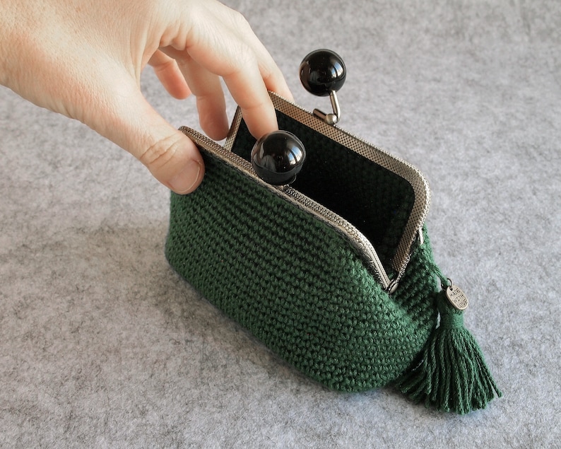 May include: A green crocheted coin purse with a black tassel and a silver clasp. The purse is open and the inside is lined with black fabric.