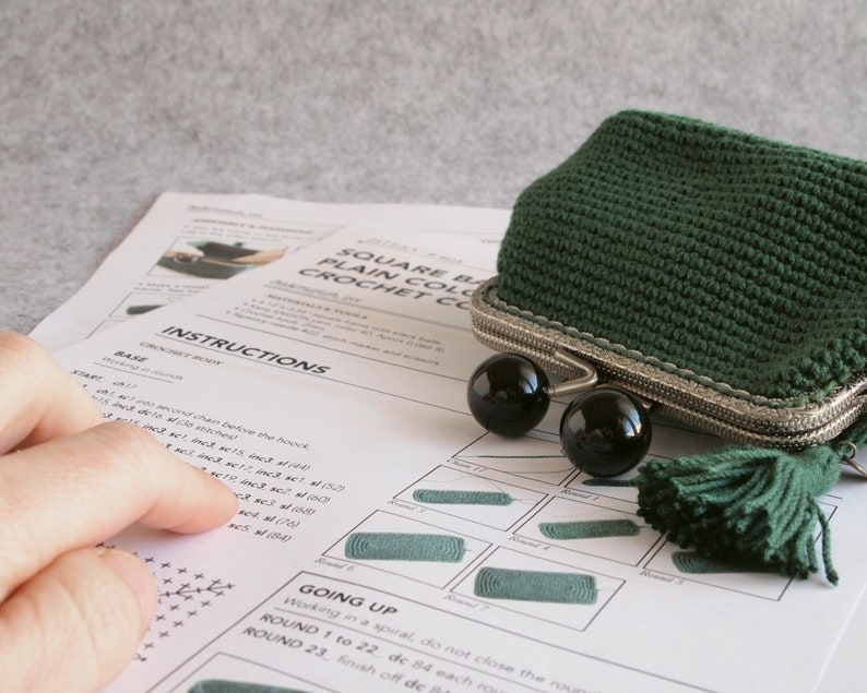 May include: Instructions for crocheting a square, green crochet coin purse with a silver clasp and black beads. The instructions include a base and going up sections. The purse is shown in the image.