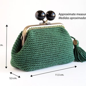 May include: A green crocheted coin purse with a metal clasp and two black beads. The purse has a tassel and measures approximately 5.5 cm wide, 9 cm tall, and 11.5 cm long.
