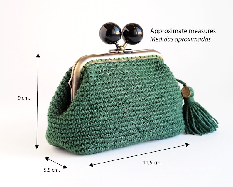 May include: A green crocheted coin purse with a metal clasp and two black beads. The purse has a tassel and measures approximately 5.5 cm wide, 9 cm tall, and 11.5 cm long.
