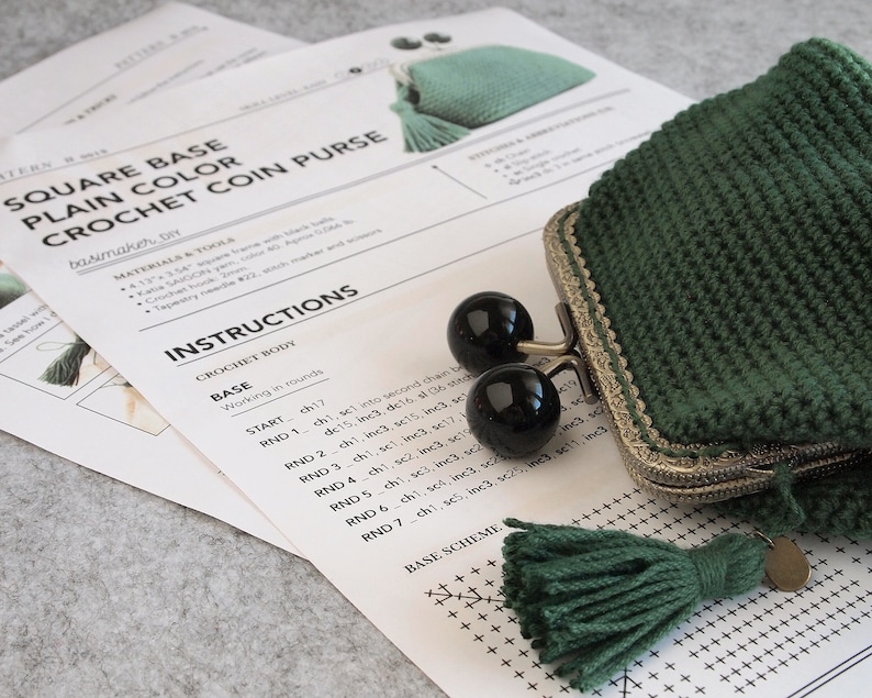 May include: A crochet pattern for a square base coin purse with instructions for crocheting the base in rounds. The pattern includes a base scheme with stitches marked in a grid. The image also shows a finished green coin purse with a metal clasp and a green tassel.