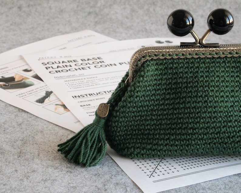 May include: A green crocheted coin purse with a metal clasp and two black round knobs. The purse has a green tassel attached to it and a tag that says "Made with Love".