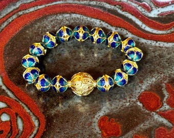 May include: A gold bracelet with blue and green enamel beads. The bracelet has a large, ornate gold bead in the center.