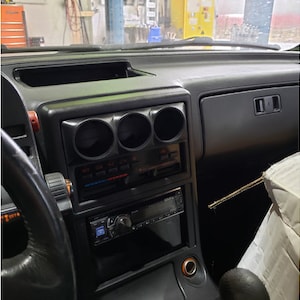 Puede incluir: El interior de un coche con un salpicadero negro y un volante negro. Hay tres indicadores redondos montados en el salpicadero. Los indicadores son negros con números y agujas blancas.