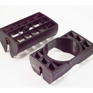 May include: Two black plastic 3D printed parts. One part is a rectangular block with a grid of holes. The other part is a ring with a grid of holes.