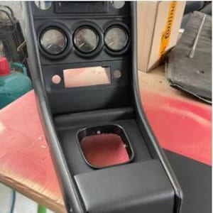 May include: Black leather car dashboard with three round gauges and a rectangular slot for a radio or other device. The dashboard has a black leather center console with a square opening for a shifter.