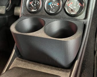 May include: A black plastic cup holder with two compartments, designed to fit into a car's center console. The cup holder is installed below a panel with three gauges, labeled "Oil", "Temp", and "Volt".