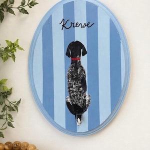 May include: An oval wooden wall plaque featuring a painted black and white speckled dog viewed from behind, wearing a red collar. The background consists of vertical light and medium blue stripes, with the word Krewe written in black script.