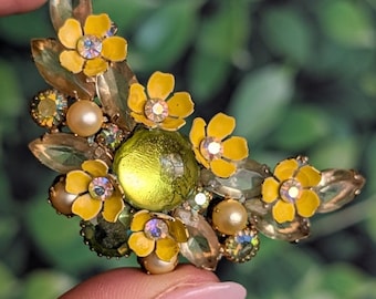 Peut inclure: Broche florale vintage avec des fleurs en émail jaune, des centres en cristal, un centre en verre vert et de fausses perles. La broche a un sertissage en métal doré et des accents de cristal transparents. Le design est en forme de croissant.