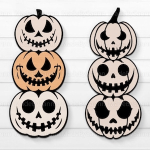Peut inclure: Deux décorations de citrouilles d'Halloween en bois empilées. Chaque citrouille a un visage sculpté avec un contour noir. Les citrouilles sont dans des tons beiges et orange, avec des traits noirs. Le fond est blanc.