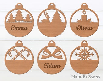 May include: Six wooden Christmas ornaments with different designs. The ornaments are round and have a flat bottom. The designs include a Christmas tree, a deer, a candle, candy canes, a bow, and a snowflake. The ornaments are personalized with the names Emma, Olivia, Adam, and MADE BY SANNN.
