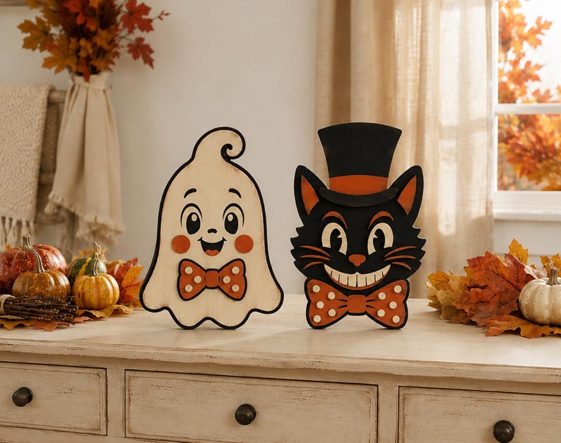 May include: Two wooden cutout decorations featuring a smiling cream-colored ghost with a polka-dot bow tie and a black cat wearing a top hat with an orange band and a matching polka-dot bow tie, both designed with a vintage-inspired aesthetic.