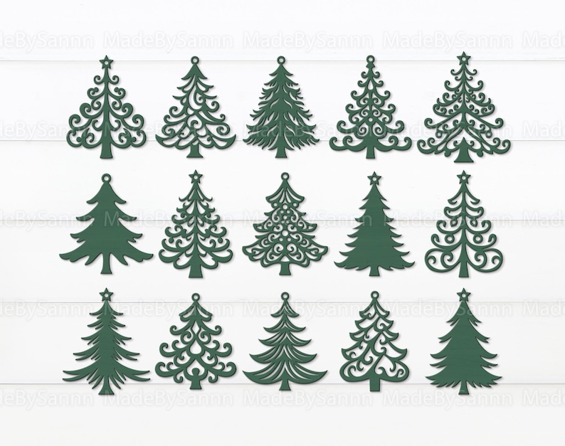 May include: A collection of dark green Christmas tree cutouts in various designs, including solid and ornate styles. Each tree has a star at the top and a small hole for hanging. The trees are arranged on a white, wood-grain background.