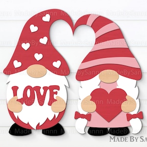 K&ouml;nnte beinhalten: Zwei Gnome, die Herzen halten. Ein Gnome tr&auml;gt einen roten Hut mit wei&szlig;en Herzen und h&auml;lt ein Schild mit der Aufschrift "LOVE". Der andere Gnome tr&auml;gt einen rosa-rot gestreiften Hut und h&auml;lt ein rotes Herz.