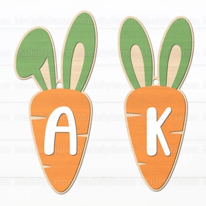May include: Two wooden carrot-shaped ornaments with bunny ears. The carrots are orange and have white letters on them. The letters are A and K.