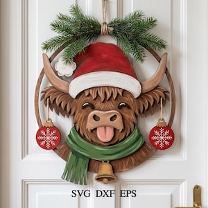 Op de afbeelding: Een gelaagde houten wanddecoratie met een bruine Schotse hooglander die een rode kerstmuts en een groene sjaal draagt. De koe steekt de tong uit en is omlijst door een houten ring met twee rode sneeuwvlokornamenten en een belletje.