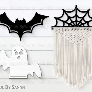May include: Three Halloween-themed wooden cutouts: a bat, a ghost, and a spiderweb. The bat is black and the ghost is white. The spiderweb is black and has a white macrame wall hanging behind it. The text "MADE BY SANNN" is at the bottom of the image.