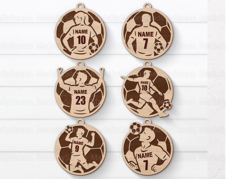 May include: Six wooden soccer-themed ornaments. Each ornament features a soccer player design with a jersey number and the word "NAME". The ornaments are circular with a soccer ball background and a hole for hanging.