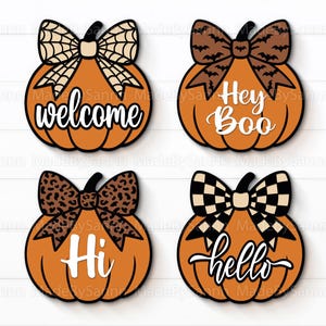 May include: Four orange pumpkin-shaped decorations with black outlines and bows. The pumpkins have different bow designs: spiderweb, bats, leopard print, and checkered. Each pumpkin has a white word: "welcome", "Hey Boo", "Hi", and "hello".