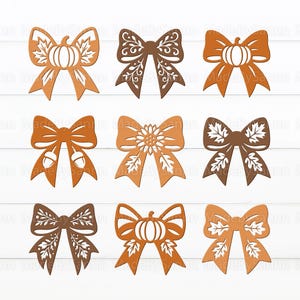 May include: Nine decorative wooden bows in shades of brown and orange, featuring fall-themed designs. The bows include pumpkin, acorn, and leaf motifs, perfect for autumn crafts and decorations. The bows are arranged on a white wooden surface.