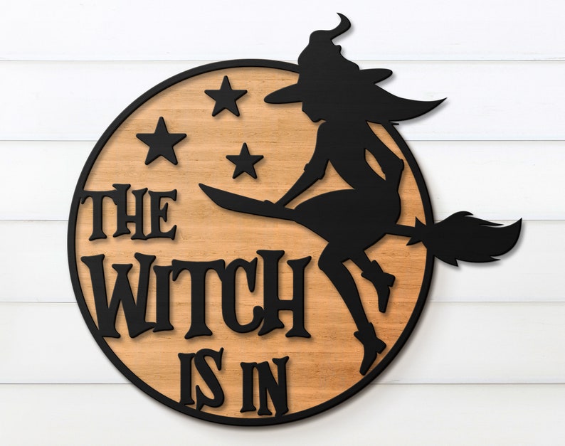 K&ouml;nnte beinhalten: Ein rundes Holzschild mit dem Text "The Witch Is In" in schwarzen Buchstaben. Eine schwarze Silhouette einer Hexe, die auf einem Besen reitet, mit Sternen im Hintergrund.
